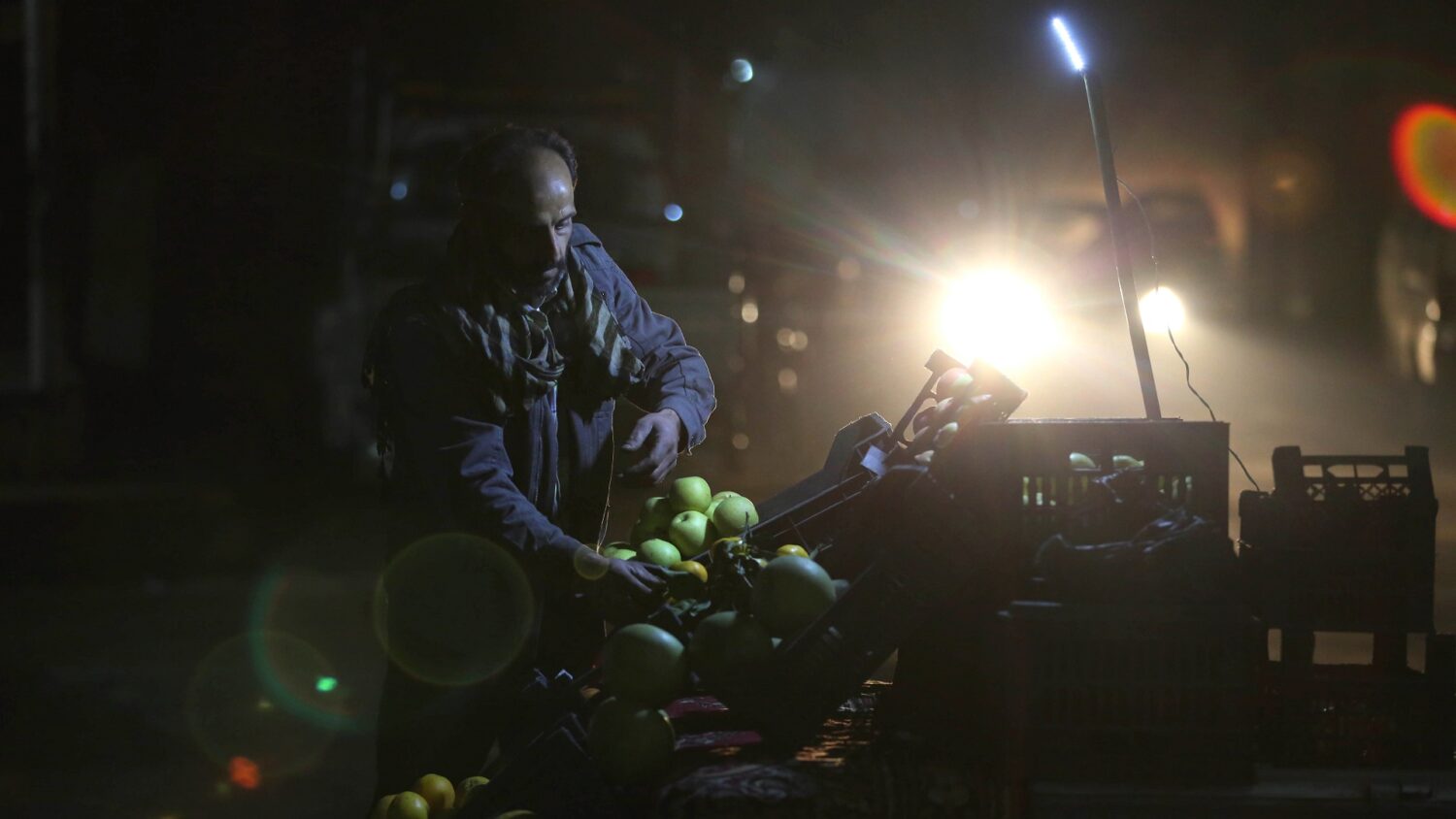 بائع سوري يرتب التفاح في كشك لبيع الفاكهة وسط انقطاع مستمر في الكهرباء - إنترنت